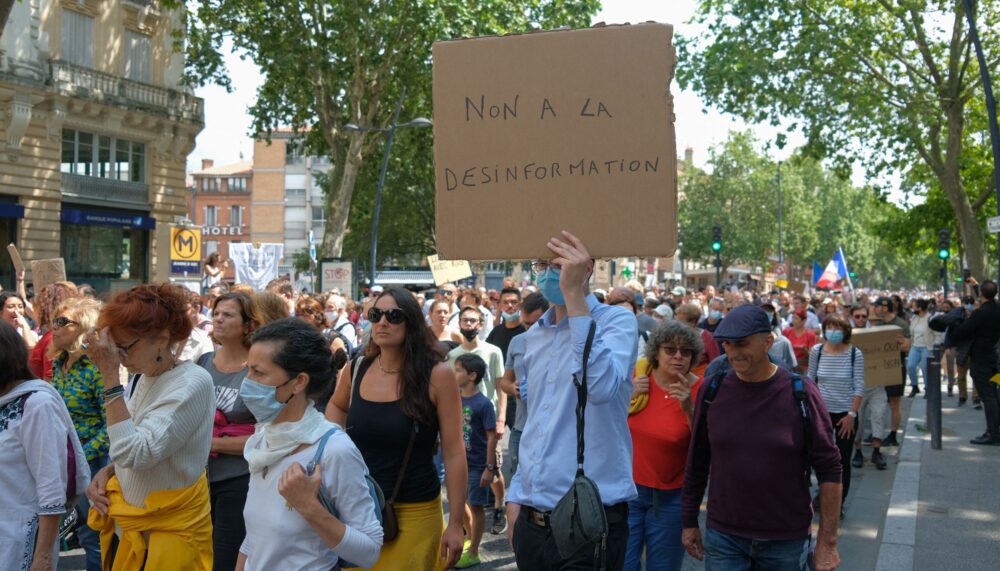 Protester with placard about disinformation. On August 7, 2021, several thousand people defied the prefectural ban on demonstrating, marching in the streets of Toulouse (France). Chanting the word "Freedom", and anti-Macron slogans, the demonstrators marched on the boulevards of the city center, thus protesting against the Sanitary Pass.